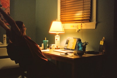 A mom entrepreneur stretching beside her laptop in a bright home office.