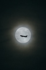 an airplane flying in the sky with the moon in the background