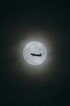 an airplane flying in the sky with the moon in the background