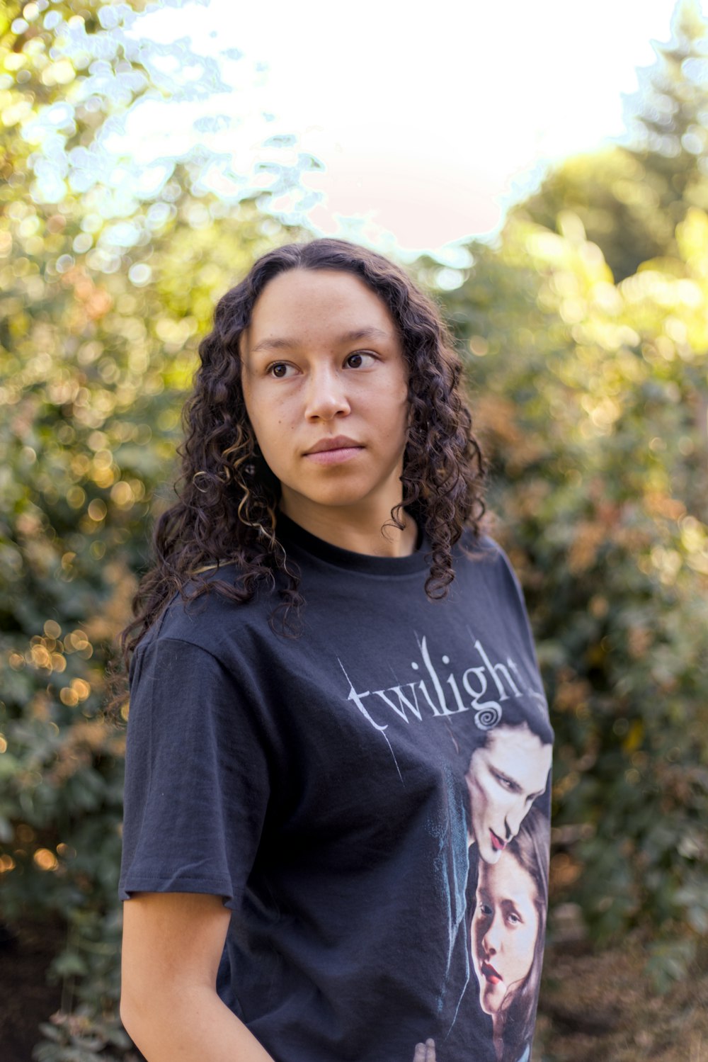 a woman with curly hair standing in front of bushes