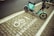 A teal electric scooter is parked on a designated bike parking area marked with white paint symbols and text in both English and Chinese. The ground consists of paved bricks, and the area appears to be part of a street sidewalk.
