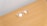 A pair of transparent eyeglasses with clear lenses is placed on a flat, light brown wooden surface. The eyeglasses are positioned at an angle, with the earpieces slightly spread apart.
