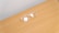 A pair of transparent eyeglasses with clear lenses is placed on a flat, light brown wooden surface. The eyeglasses are positioned at an angle, with the earpieces slightly spread apart.
