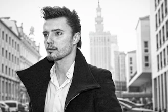 Editorial black-and-white portrait of a male model wearing streetwear in a cityscape.