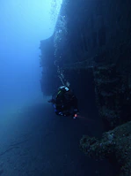 Underwater technician repairing equipment near a shipwreck.