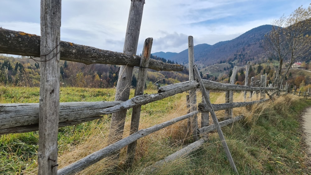 a wooden fence in a field with mountains in the background