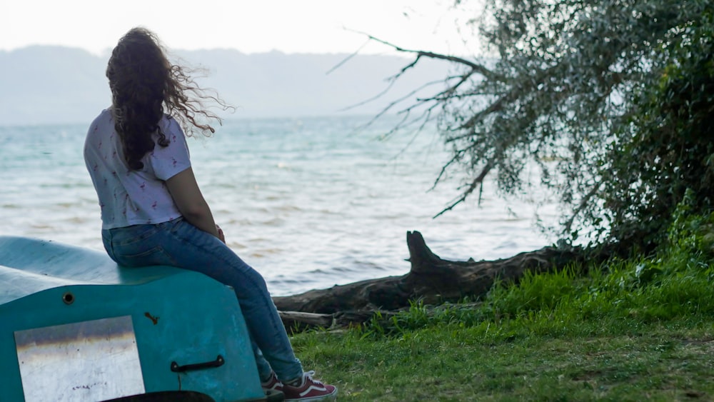 a woman sitting on a bench next to a body of water