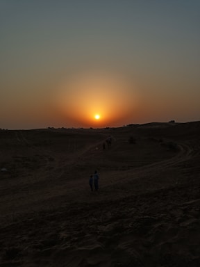 A warm sunset over a Moroccan desert with film equipment silhouettes in the foreground.