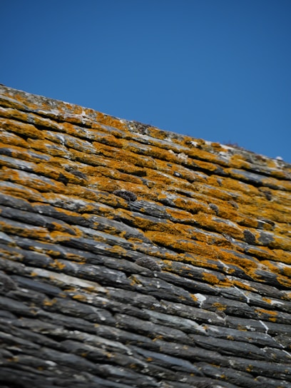 Skilled roofer repairing a slate roof under a clear blue sky.