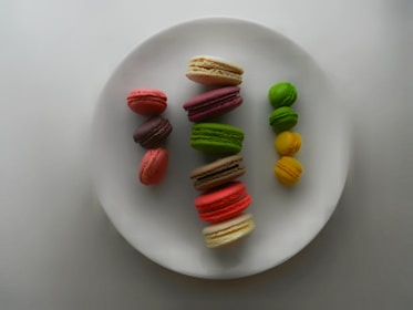 An array of colorful macarons arranged neatly on a vintage ceramic plate, showcasing vibrant pistachio green, ruby red, and creamy vanilla hues.