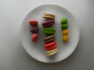 An array of colorful macarons arranged neatly on a vintage ceramic plate, showcasing vibrant pistachio green, ruby red, and creamy vanilla hues.