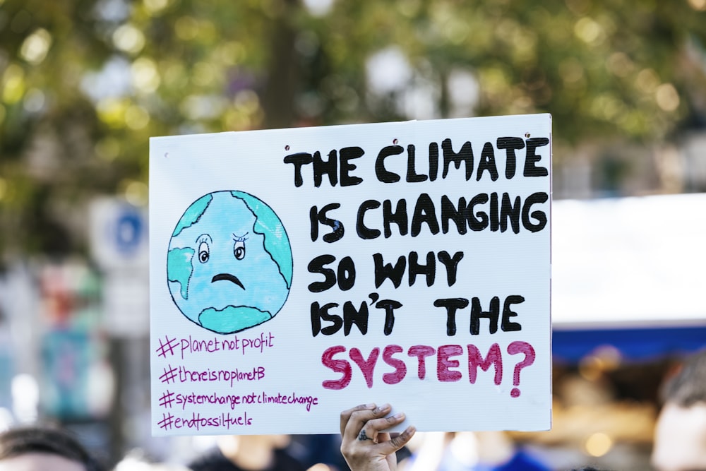 una persona que sostiene un cartel que dice que el clima está cambiando, así que ¿por qué no lo está haciendo?
