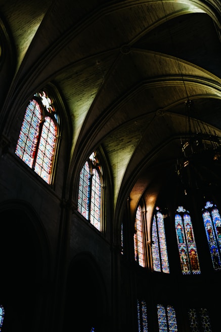 Intergenerational worship with hands raised, bathed in soft emerald light from stained glass.
