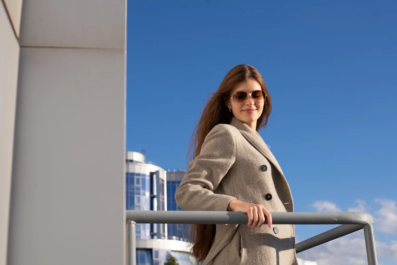 stylish woman in coat and sunglasses leaning casually