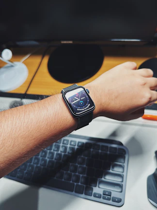 A smiling IT professional wearing a sleek custom watch while working at a modern desk.