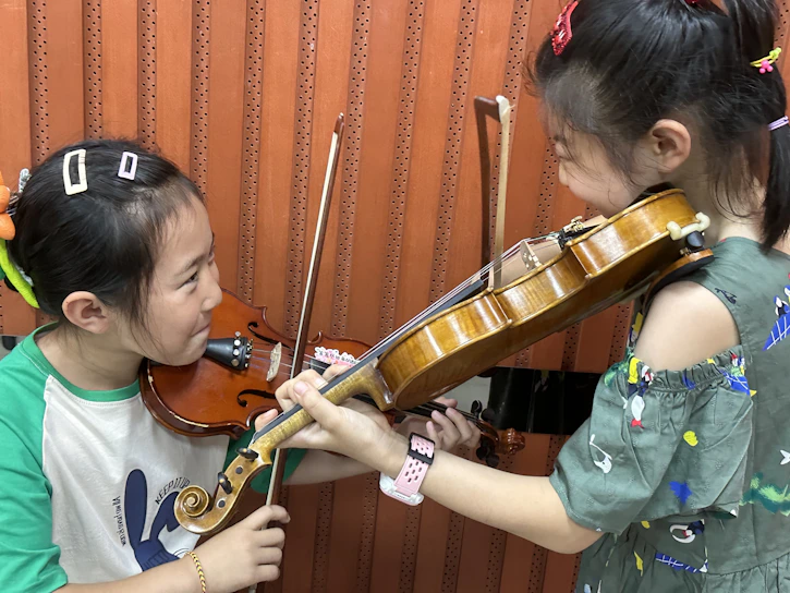 Children joyfully playing violins in a sunlit community center.