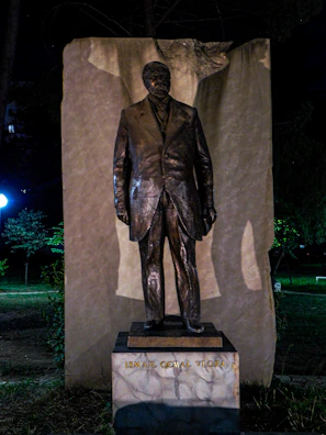 Bust of a modern Albanian historical figure with a blurred city backdrop.