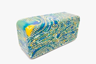 A rectangular block featuring a marble pattern with intricate swirls. The design incorporates vibrant colors such as green, blue, and yellow. The surface has a unique texture, suggesting a potential material like foam or rubber.