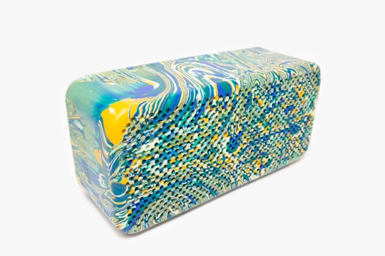 A rectangular block featuring a marble pattern with intricate swirls. The design incorporates vibrant colors such as green, blue, and yellow. The surface has a unique texture, suggesting a potential material like foam or rubber.