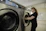 A happy customer installing a sleek, rust-resistant washing machine stand in a bright, modern laundry room.