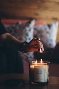 Close-up of a hand lighting a scented candle from a gold-accented jar.