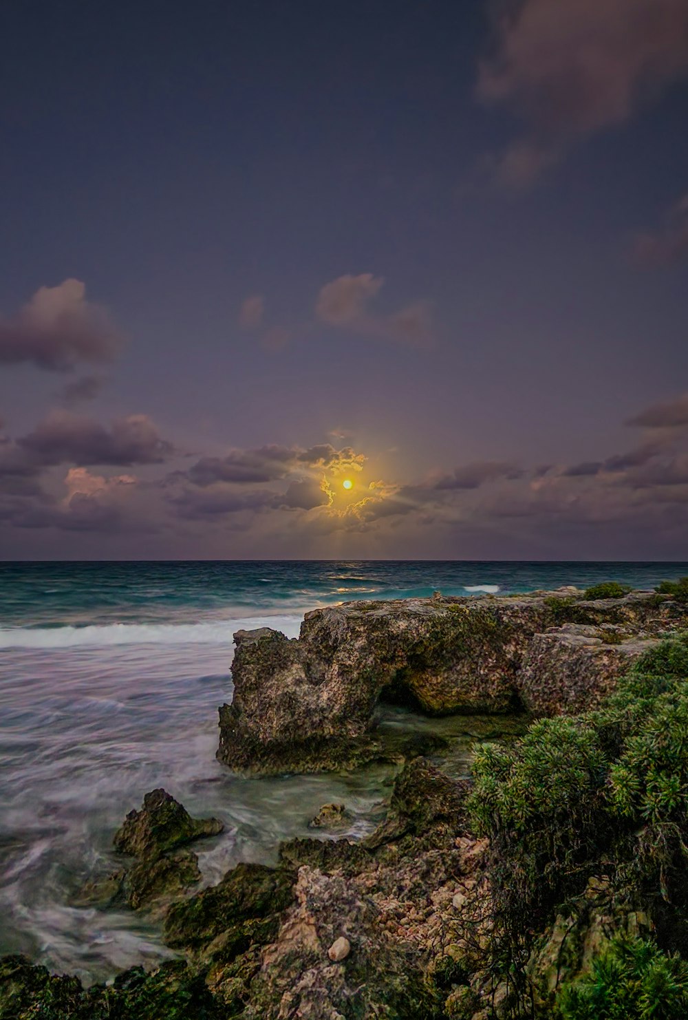 a full moon setting over the ocean and rocks
