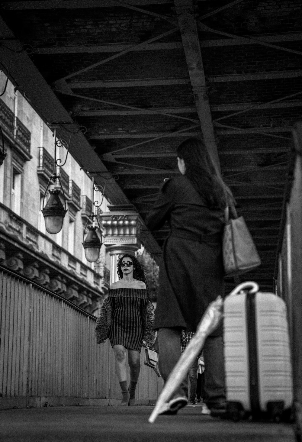 two women walking under a bridge carrying luggage