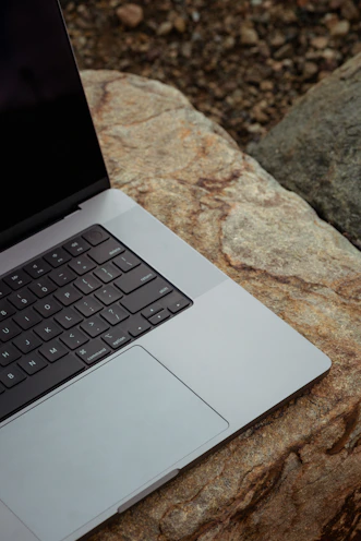 A sturdy laptop with rugged design outdoors on a rock beside a hiking backpack.