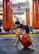 A child in athletic wear is practicing a balance exercise on the gym floor, while an instructor or coach assists nearby. Large orange punching bags are visible in the mirrored background, reflecting the gym setting.