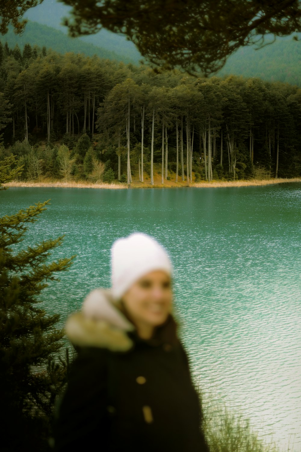 a woman standing next to a lake with a forest in the background