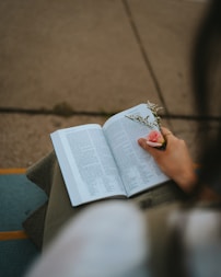 a person sitting down reading a book and holding a flower