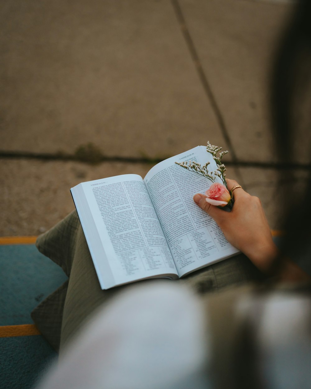 eine Person, die sich hinsetzt, ein Buch liest und eine Blume in der Hand hält