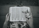 A close-up of hands holding a well-worn Bible with a delicate flower pressed inside.