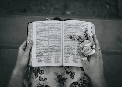 A close-up of hands holding a well-worn Bible with a delicate flower pressed inside.