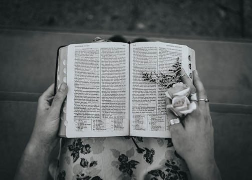 Hands holding a well-worn Bible with a delicate flower pressed inside.