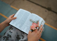 Hands adorned with rings holding a vintage book, blending timeless style with modern grace.