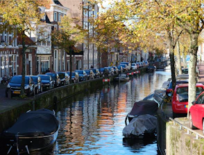 A sleek taxi parked by an iconic Amsterdam canal at sunset.