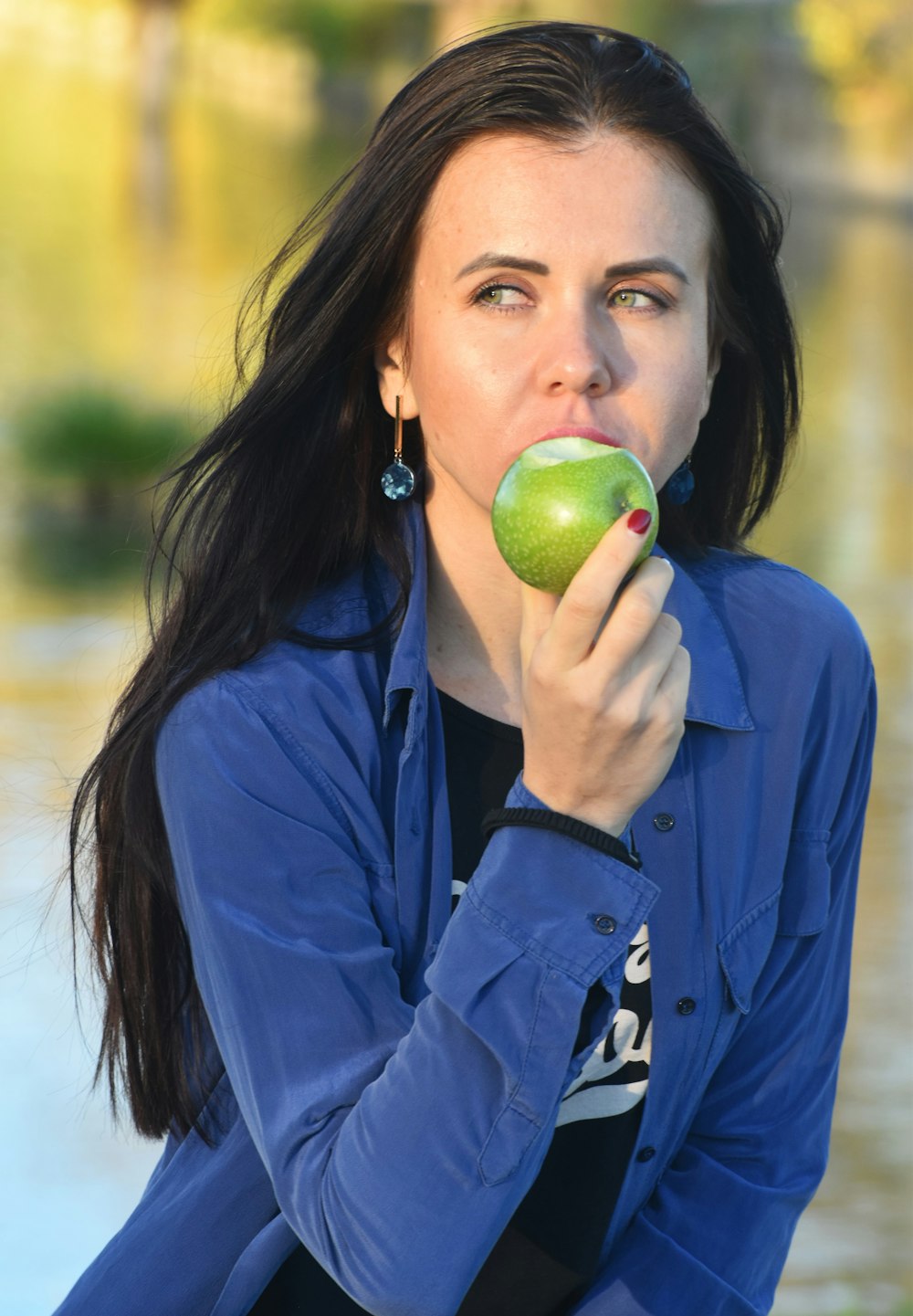 a woman in a blue shirt eating an apple