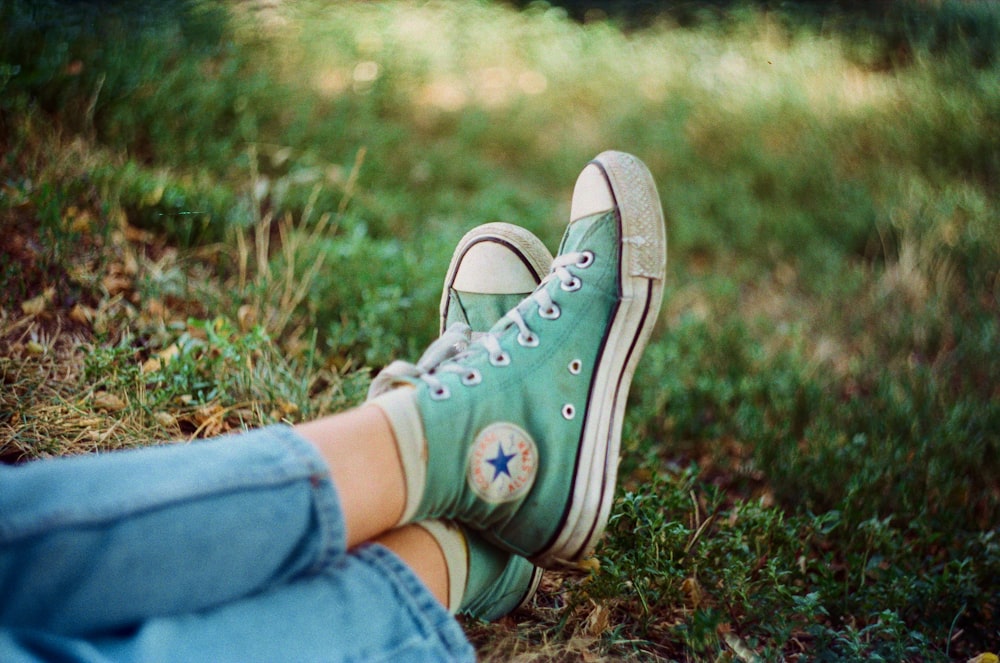 a person wearing green converse shoes sitting in the grass