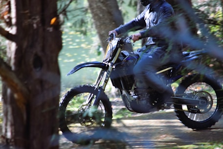 A dynamic shot of a motocross rider kicking up dirt on a rugged forest trail under moody skies.