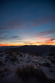 A cinematic image of a rugged outdoor landscape with bronze-hued rocks and a deep petrol blue sky at dusk.