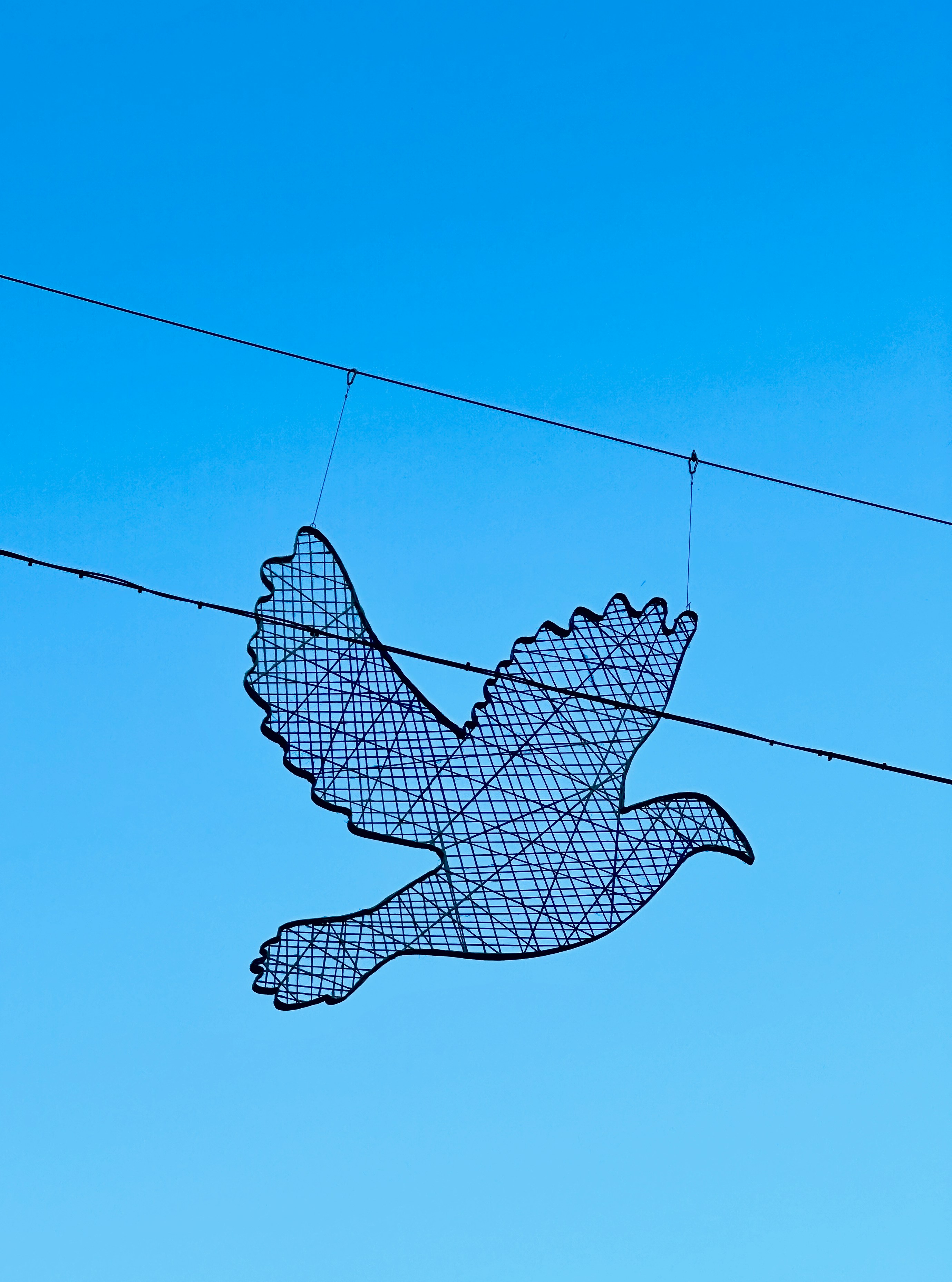 Eine Skulptur eines Vogels auf einem Draht vor einem blauen Himmel