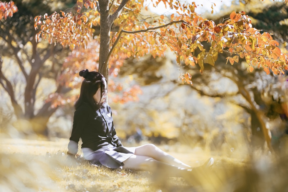 a woman sitting in the grass under a tree