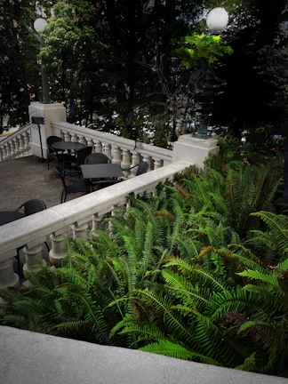 A sophisticated outdoor terrace with black wrought iron furniture and gold lanterns overlooking a serene garden.