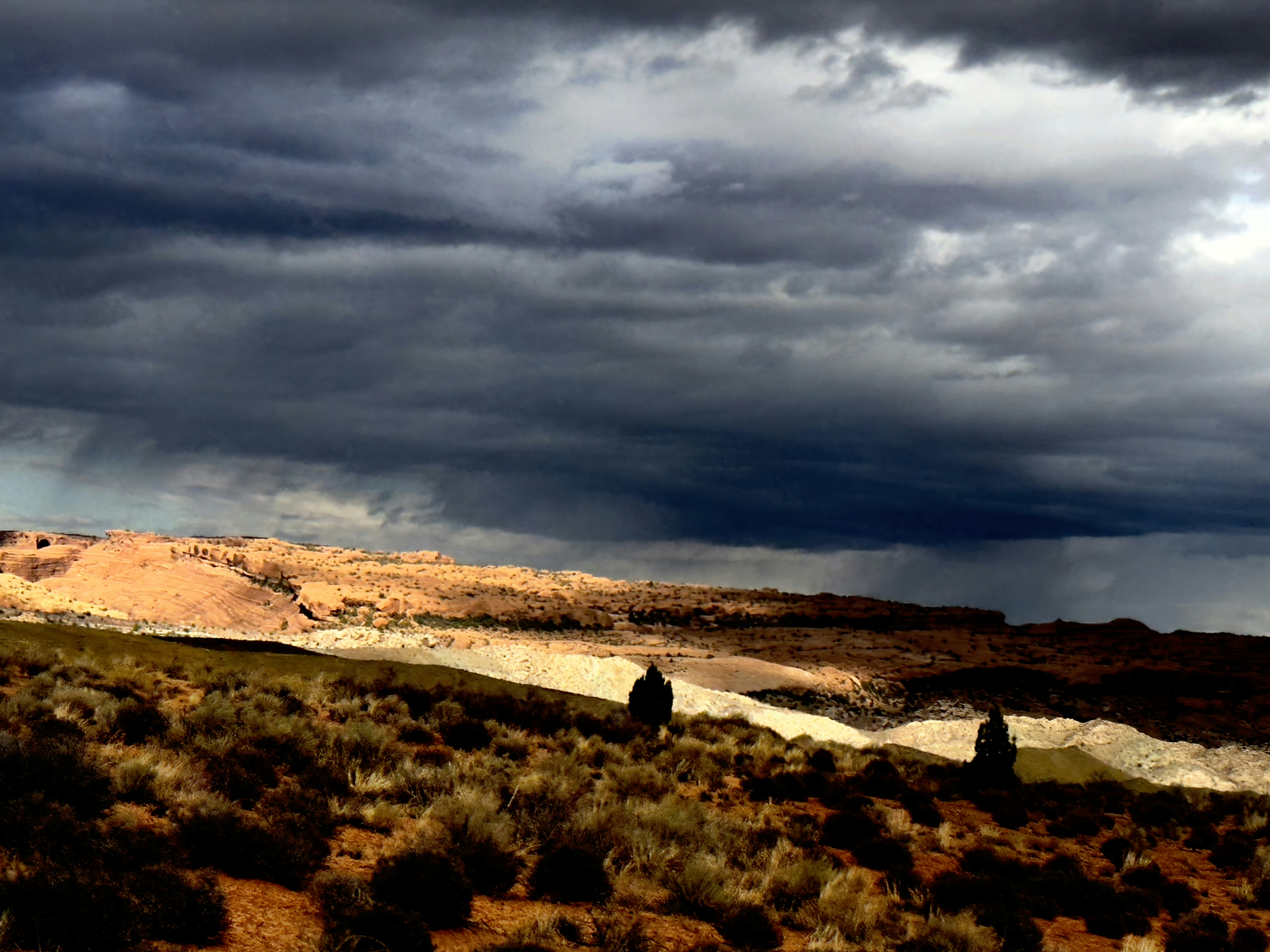 a couple of people walking across a field under a cloudy sky