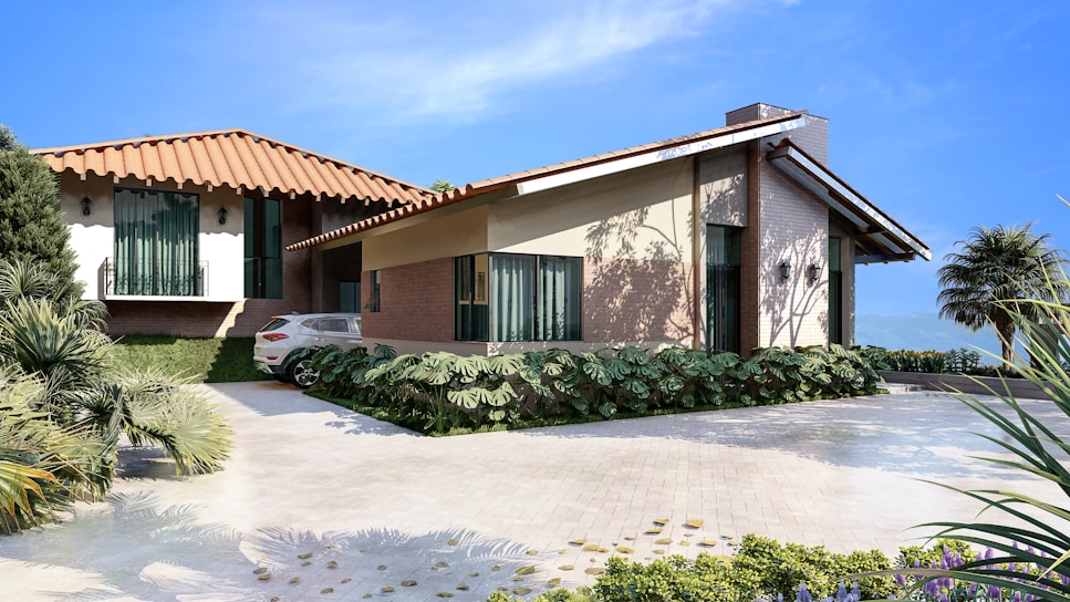A modern house with a red-tiled roof and beige walls is situated in a landscaped setting. The driveway features neatly trimmed greenery and a parked white car. The blue sky and distant mountains create an inviting and serene ambiance.