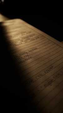 A notebook page filled with handwritten notes, partially illuminated by a soft light. The content on the page appears to relate to HTML or coding, with tags and attributes visible. The lighting creates a warm and focused atmosphere, with shadows casting over parts of the page.