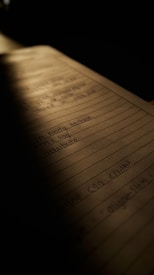 A notebook page filled with handwritten notes, partially illuminated by a soft light. The content on the page appears to relate to HTML or coding, with tags and attributes visible. The lighting creates a warm and focused atmosphere, with shadows casting over parts of the page.