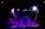 A dimly lit stage with vibrant lighting effects, including spotlights in shades of blue, purple, and white. The central feature is a stone-like archway surrounded by layered platforms. Smoke or mist creates a mystical atmosphere.