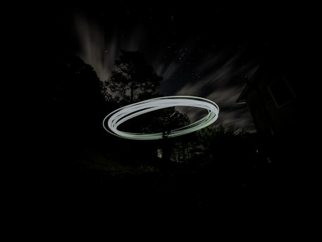 A mysterious glowing UFO hovering silently over a dark forest at night.